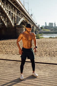 Muscular man exercising outdoors near a riverside bridge on a sunny day.