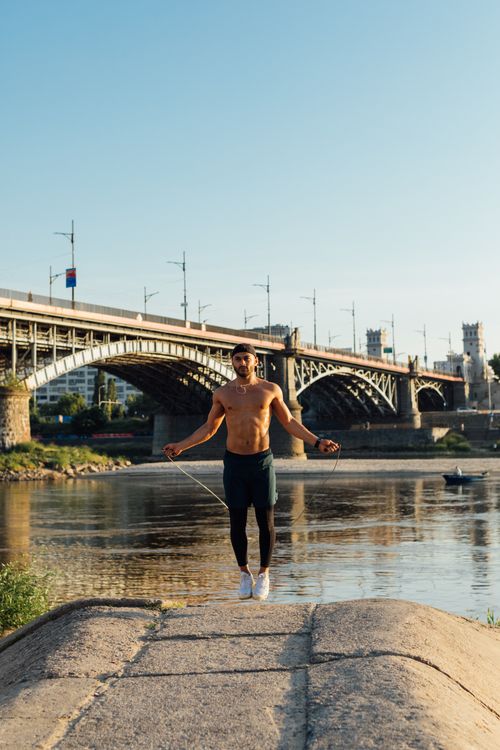 Free A man exercising with a skipping rope on a riverside path near an urban bridge. Stock Photo