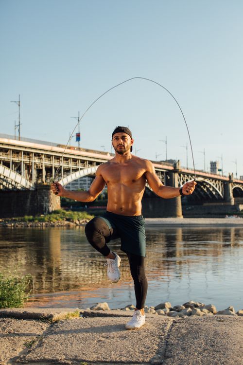 Free Fit man skipping rope outdoors near a bridge on a sunny day, exuding energy and determination. Stock Photo
