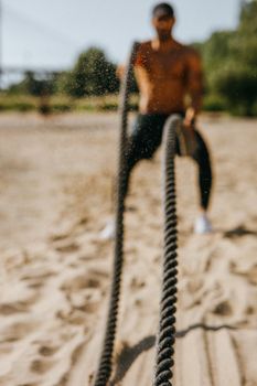 Man training with battle ropes on a sandy beach, showcasing strength and determination.