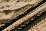 Close-up of heavy black battle ropes on a sunlit sandy beach, emphasizing texture.
