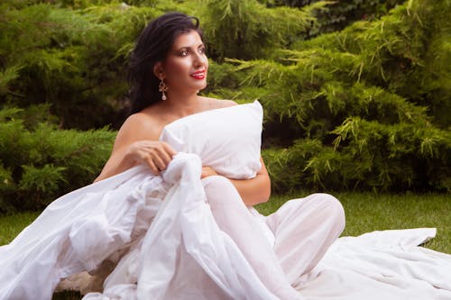 Free An Elegant Woman in White Dress Sitting on a Grassy Field Stock Photo