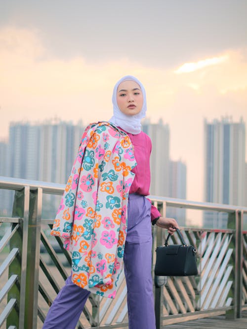A Pretty Woman in Floral Hijab Standing while Holding a Black Handbag