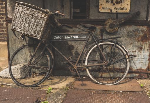 An old rusty bicycle with wicker basket leans against a vintage wall in an urban setting, evoking nostalgia.