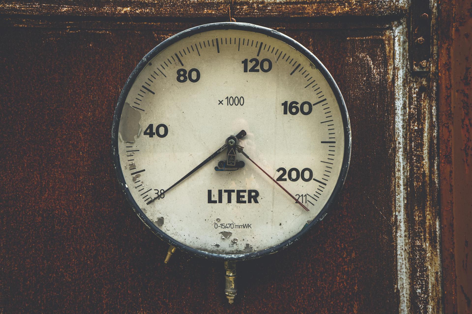 Close-up of a vintage analog gauge displaying liters on a rustic metal background.