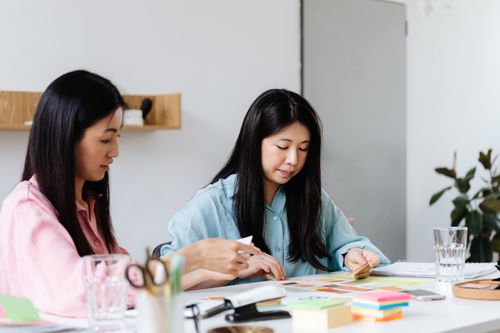 Free Two women collaborate on a project in a modern office setting, surrounded by colorful stationery. Stock Photo