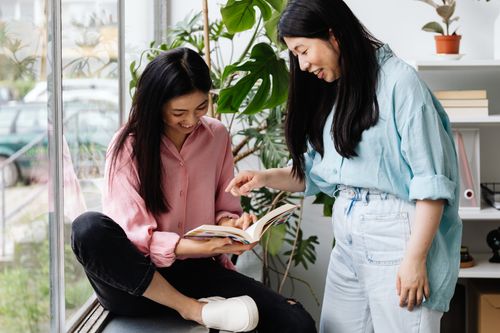 Free Two women sharing a moment while reading a book together indoors. Stock Photo