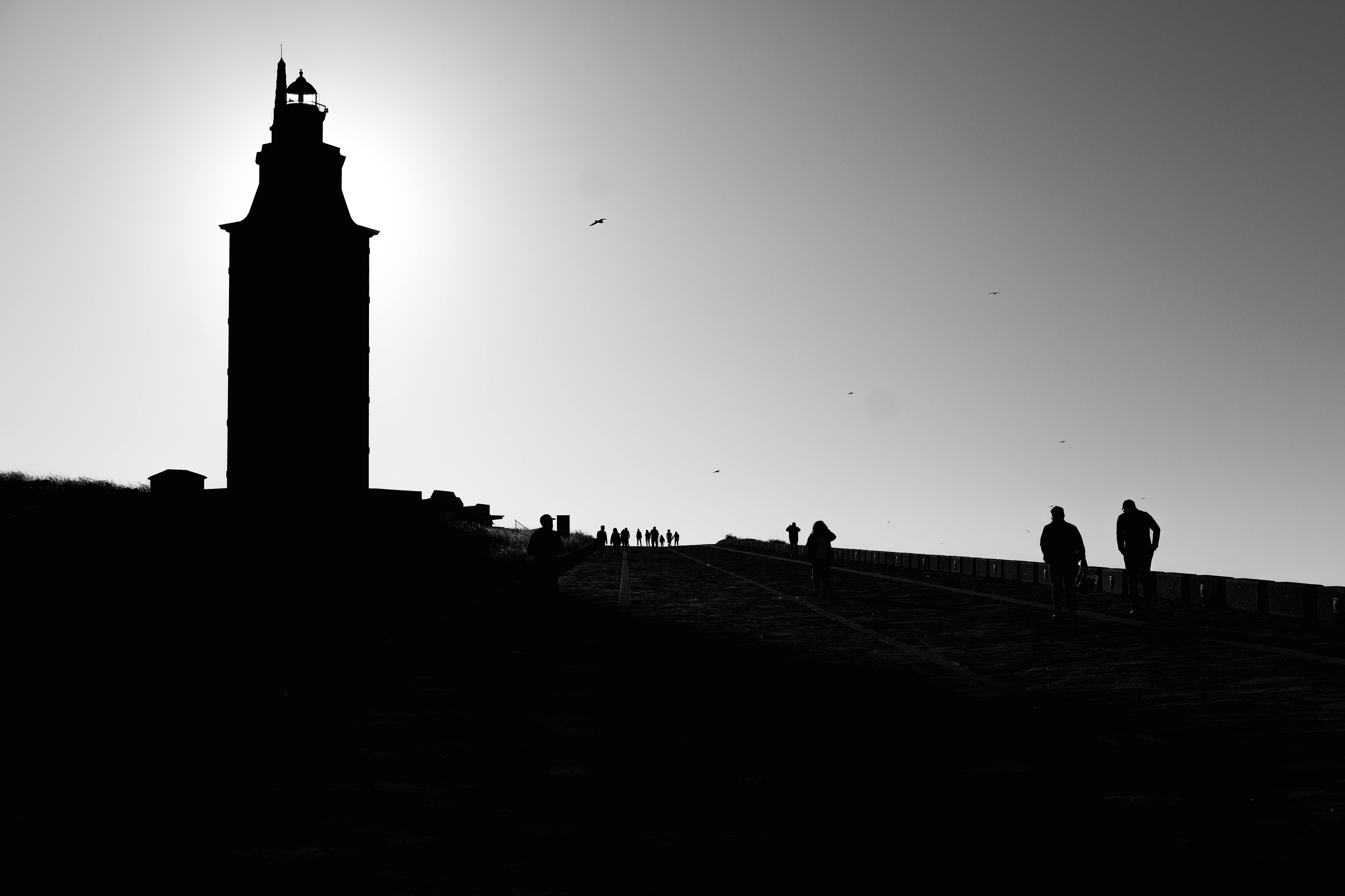 Silhouettes walking towards the Tower of Hercules during sunrise in A Coruña, Spain.