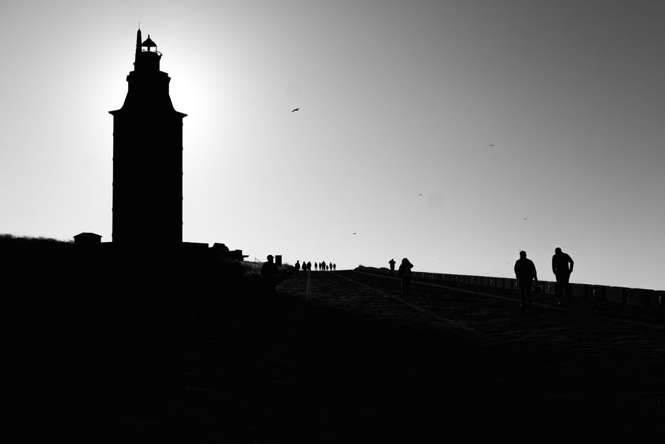 Silhouettes walking towards the Tower of Hercules during sunrise in A Coruña, Spain.
