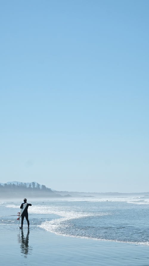 Person Standing on Seashore Under Clear Blue Sky