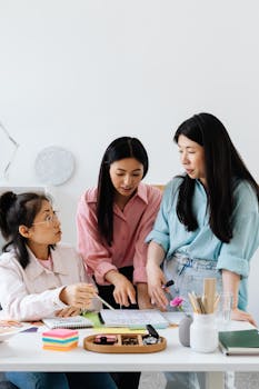 Three Asian women engaged in a collaborative discussion around a table with documents and stationery.