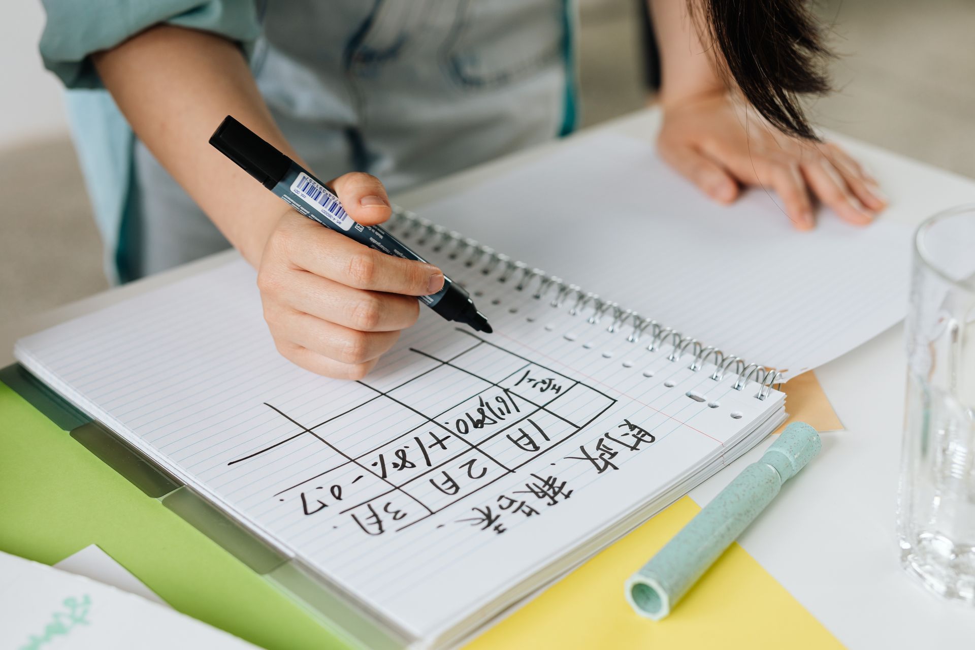 Focused woman writing a table chart in a spiral notebook on a desk, planning her tasks.