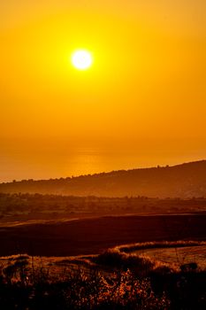 Serene landscape with golden sunset lighting up the horizon over rolling hills and ocean.