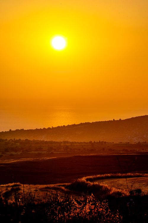 Free Serene landscape with golden sunset lighting up the horizon over rolling hills and ocean. Stock Photo