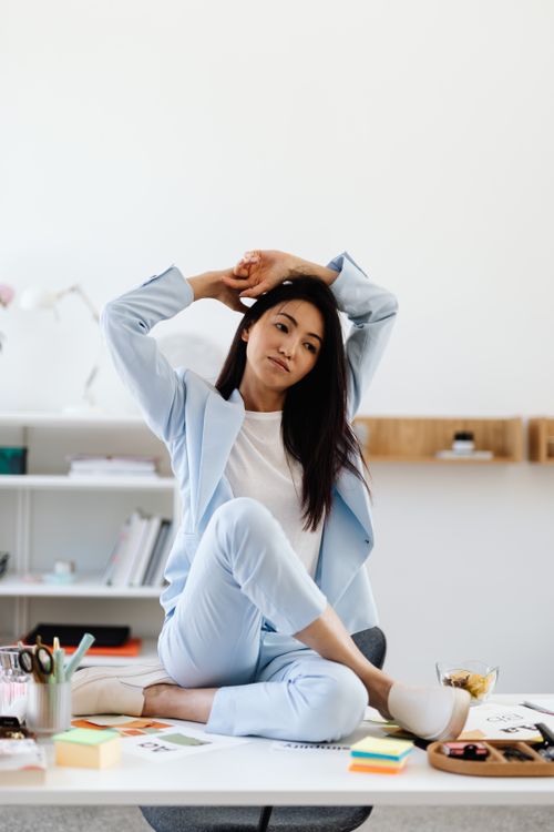 Free A relaxed businesswoman in a light blue suit stretches on a desk in a contemporary office setting. Stock Photo