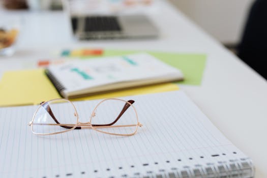 Close-up view of eyeglasses on a notebook, with colorful documents on a tidy desk setup.