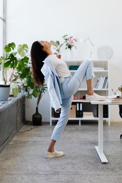 Free Business woman in blue suit stretching in bright office space, promoting workplace wellness. Stock Photo