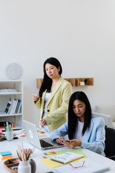Two women in a contemporary office space working on a laptop and smartphone.