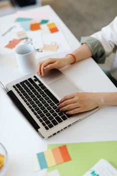 Young woman using a laptop at a bright, modern office desk with stationery and a coffee cup.