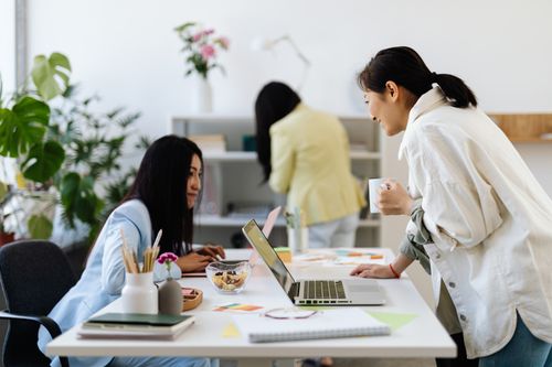 Free Three women collaborate in a modern office setting, using laptops and sharing ideas. Stock Photo