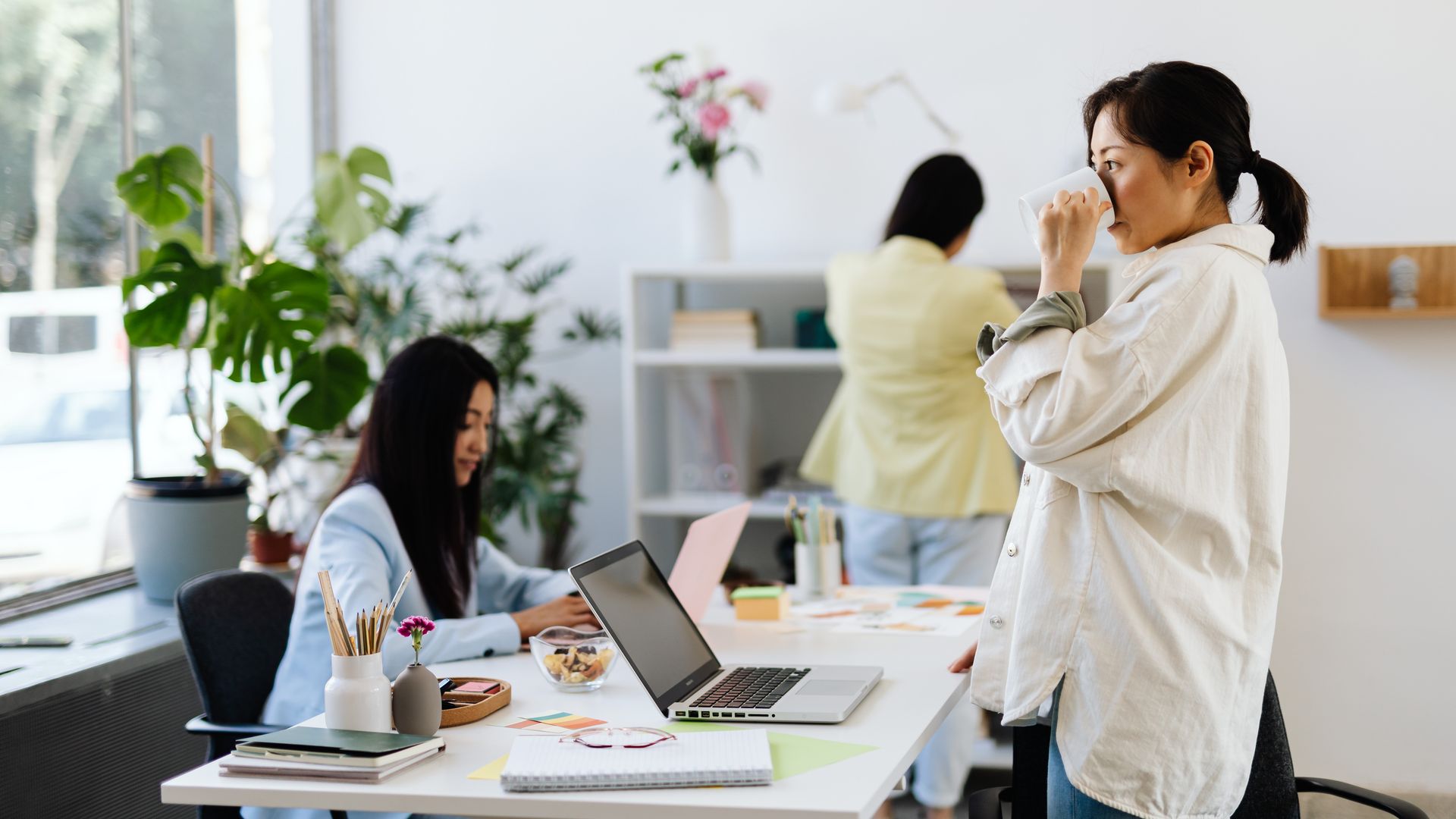 Nootropics for Work Performance: Enhance Your Productivity Three women in a modern office, working and interacting with laptops and plants around — nootropics for work performance