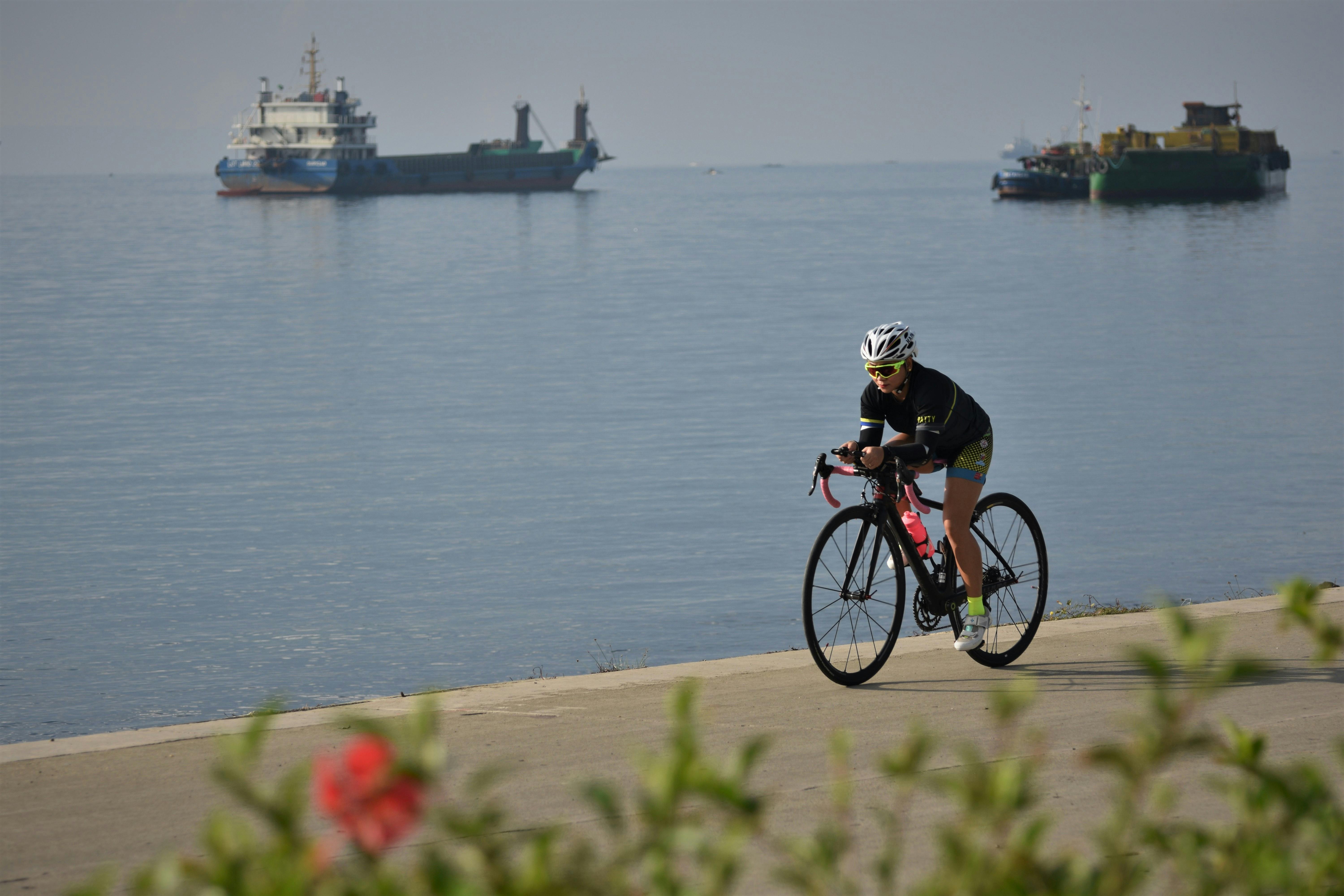 Cyclist on East Coast Park coastal path with sea view and passing cargo ships in Singapore