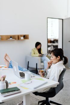 Young woman snacking while working barefoot with laptop at a stylish office desk.