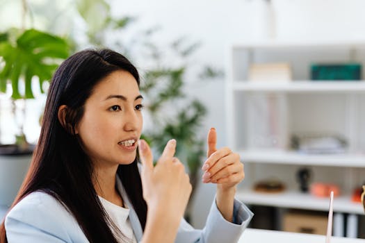 Asian woman gesturing in conversation in a modern office setting, showcasing communication.