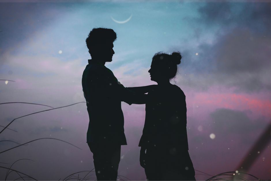 Silhouetted couple embracing under a crescent moon during twilight, creating a romantic scene.
