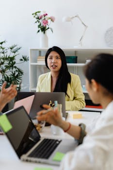 Three women working together in a modern office environment with laptops and plants.