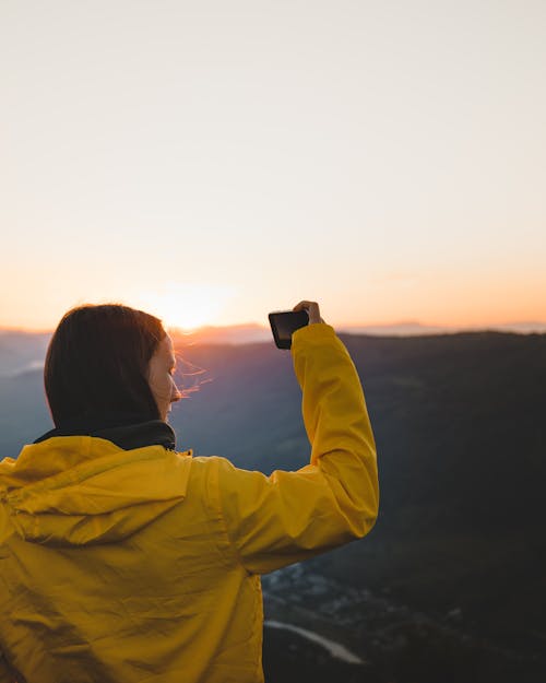 Woman in Yellow Hoodie Taking a Picture Using Phone 