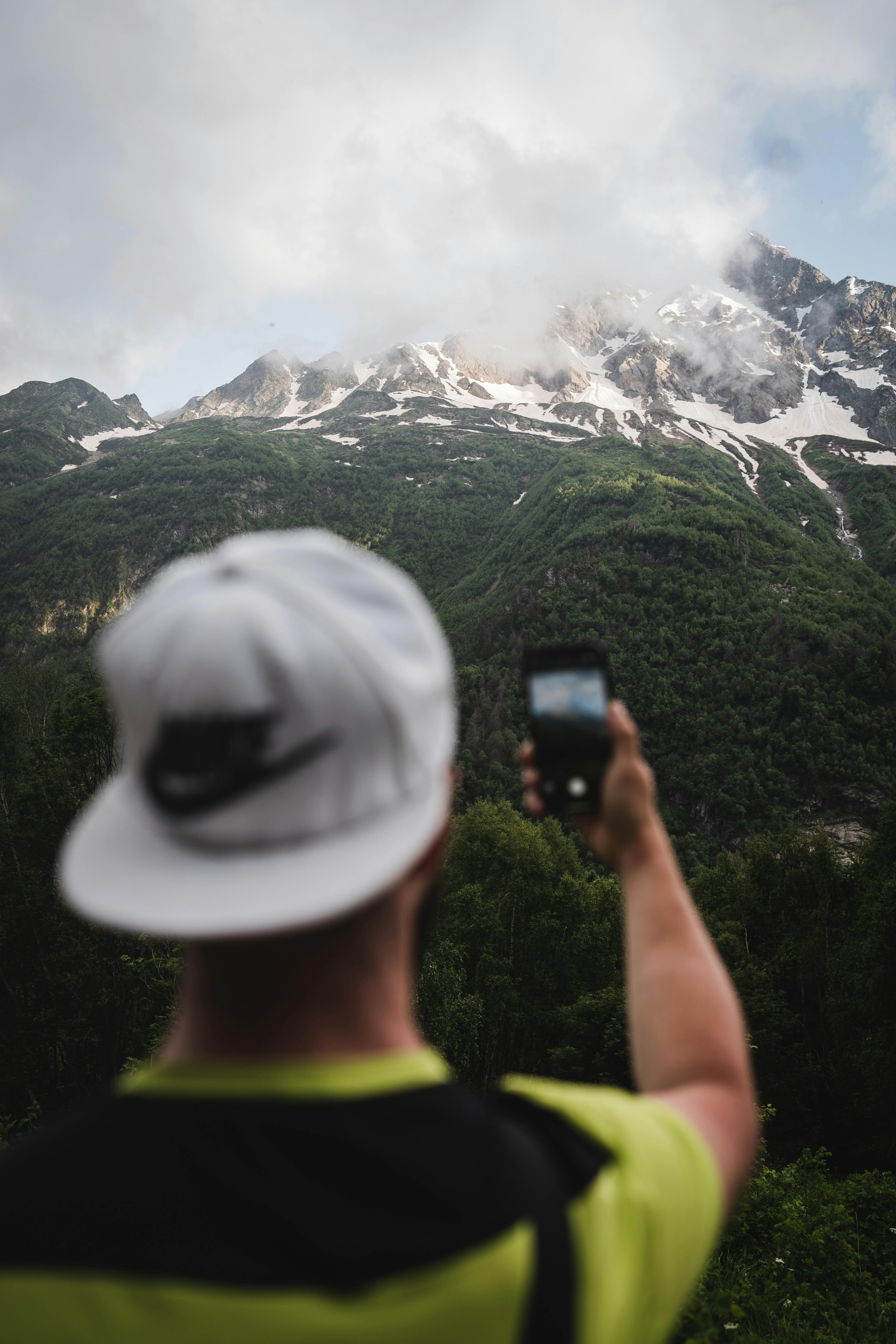 Prescription Goggle Inserts - Man photographing misty snow-capped mountains using a smartphone outdoors.