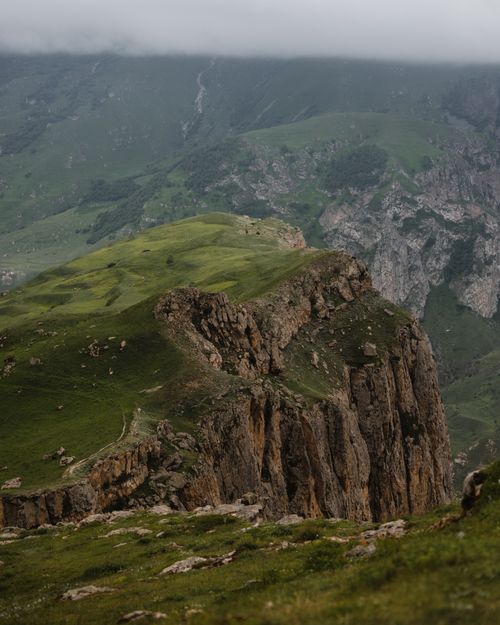 Free Captivating view of a rugged mountain cliff surrounded by lush green hills and misty skies. Stock Photo