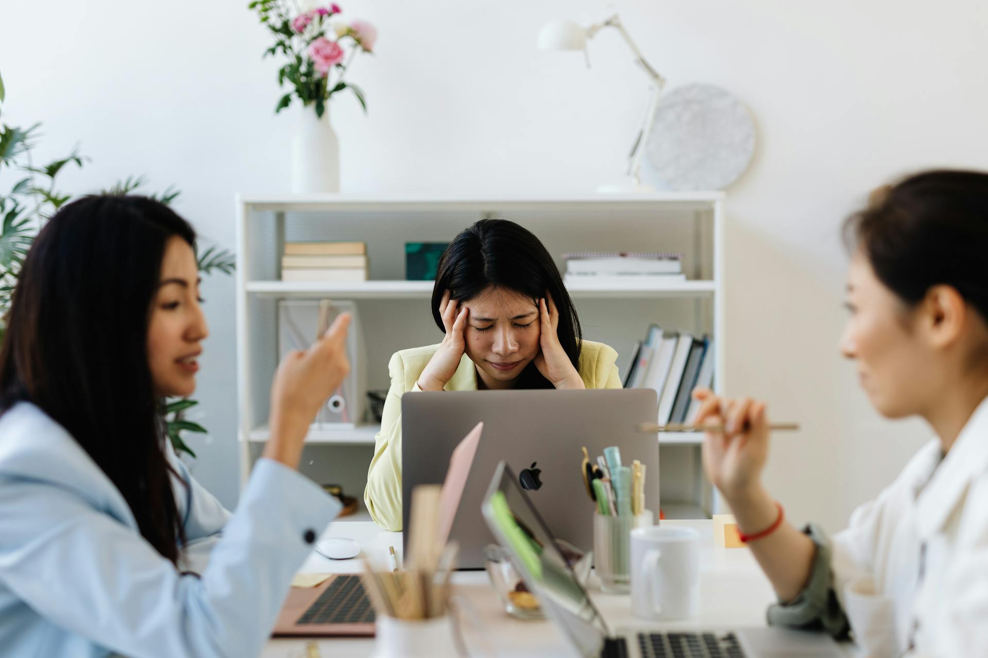 Asian businesswoman dealing with job stress in a modern office environment, surrounded by colleagues.