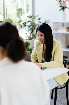 Asian woman with long black hair working on a laptop in a modern office setting.