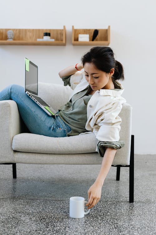 Woman Sitting On An Armchair Using Laptop and Having Coffee