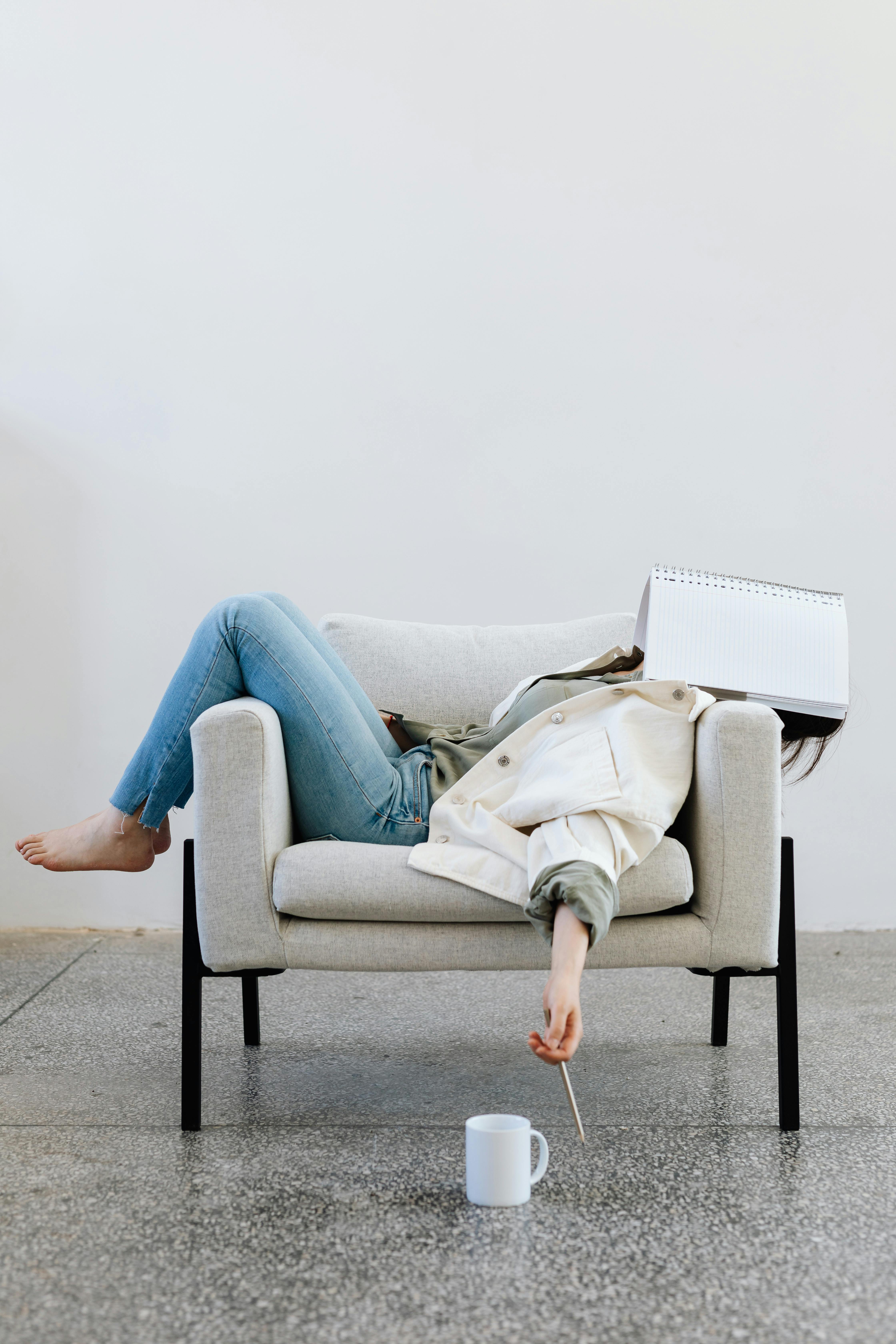 woman lying on a sofa with a notebook on her face