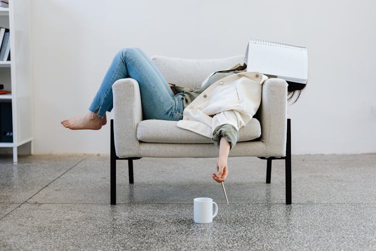 Person Lying On A Sofa With A Notebook On Her Face 