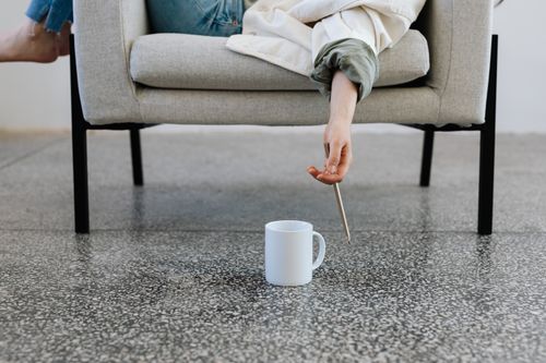 Free A person casually relaxes on a sofa, reaching for a ceramic mug using a pencil. Stock Photo