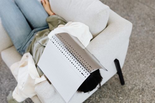 Free Woman sleeping on sofa with a notebook on her face, indoors setting. Stock Photo