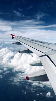 High-altitude view of an airplane wing flying over fluffy white clouds.