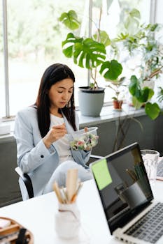 Asian woman in office attire enjoying a healthy salad during lunch break surrounded by plants.