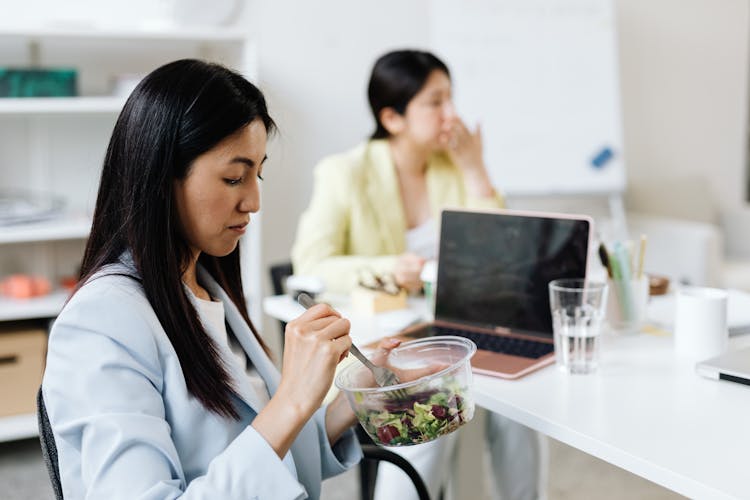 A Woman In A Blue Blazer Eating Salad In The Office