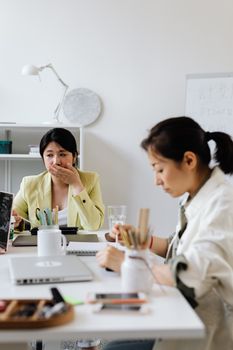 Two women working together in a modern office, one covering her mouth during a discussion.