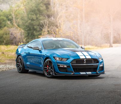 Stunning blue Mustang Shelby GT500 with white racing stripes on a scenic road.