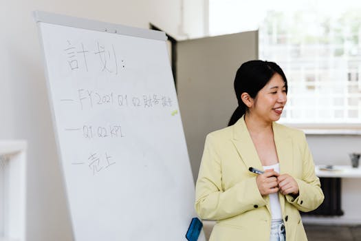 Asian businesswoman presenting a strategic plan on a whiteboard during a workplace meeting.
