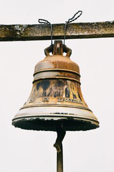 A weathered metal bell hanging on a wooden beam with rustic charm.