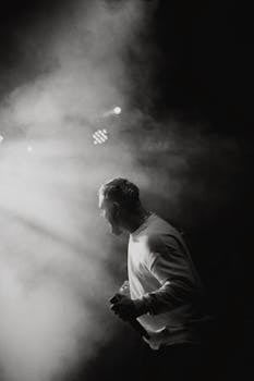 Black and white image of a male singer performing passionately on stage under dynamic lighting.