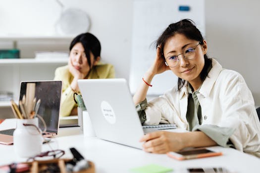 Two women working on laptops in a modern office environment, focusing on collaboration.