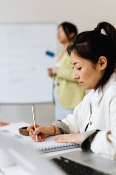 Focused Asian woman taking notes during a meeting in an office setting.